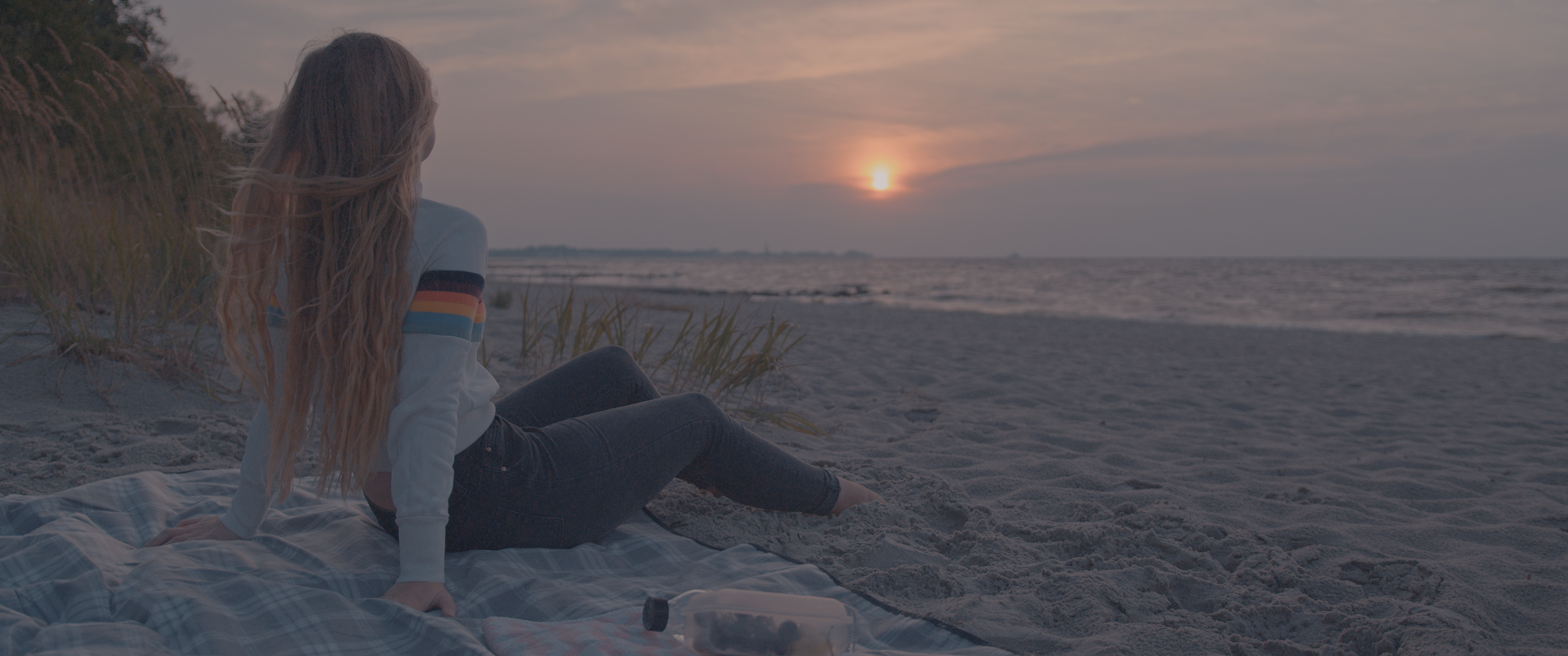 Ein Mädchen sitzt auf einer Picknickdecke am Strand und schaut sich den Sonnenaufgang an