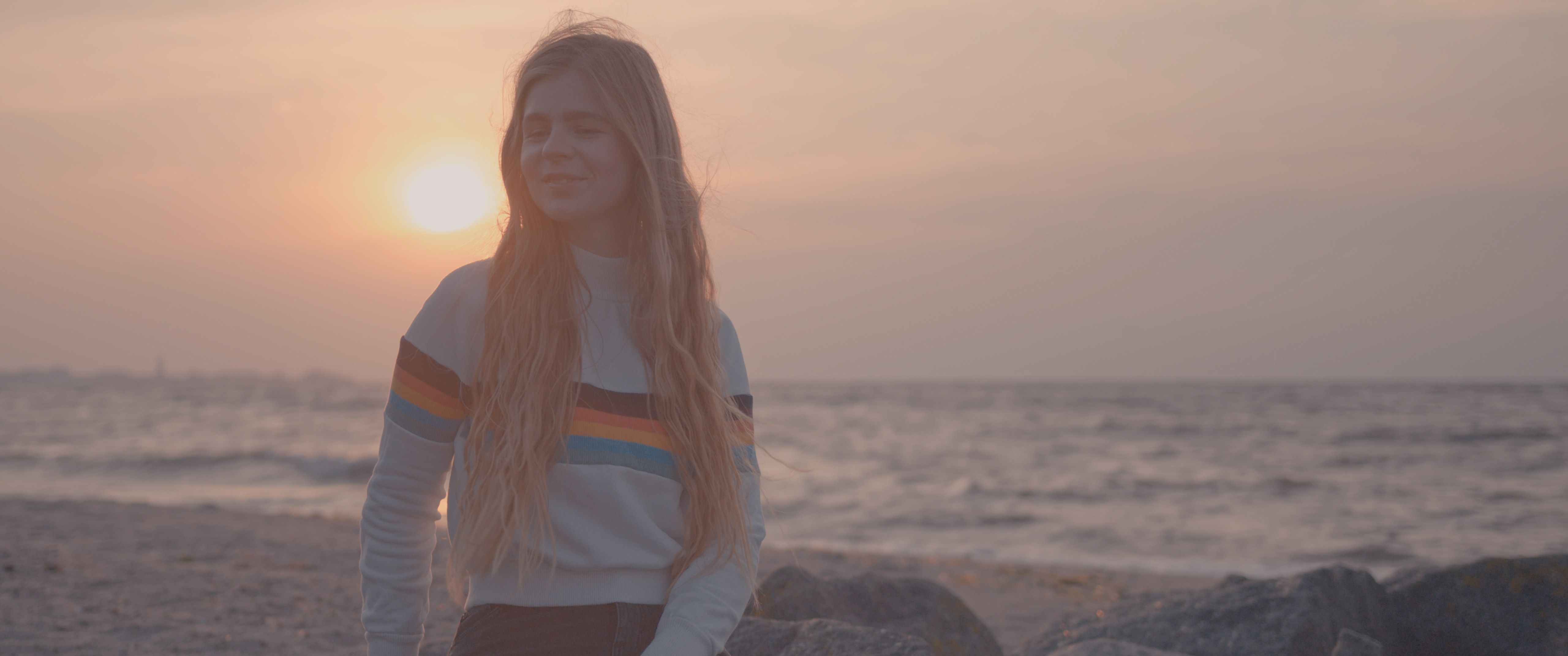 Ein Mädchen sitzt auf einem Felsen am Strand und wird vom Sonnenaufgang im Hintergrund beleuchtet