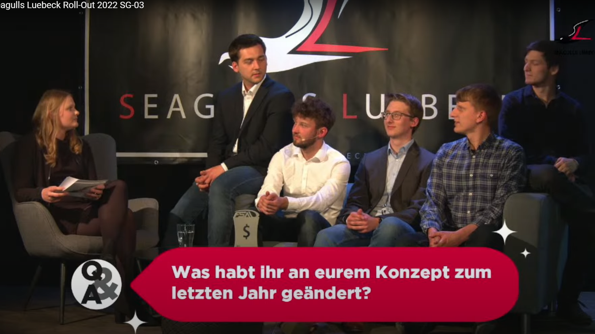 Ein Beispielbild aus dem Livstream, das Teammitglieder auf einer Couc zeigt, im Vordergrund eine eingeblendete Frage aus dem Online-Publikum